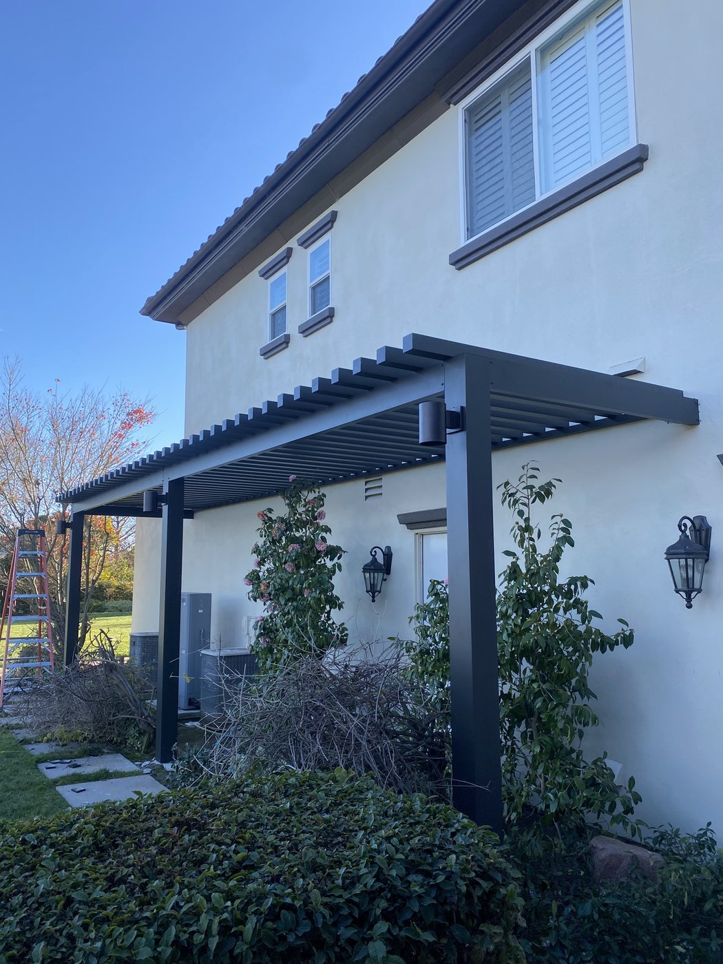 4K black louvered patio cover attached to a stucco home