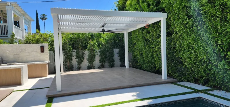 All-white freestanding 4K frame and posts with white Solara adjustable louvers and a ceiling fan, beside a pool